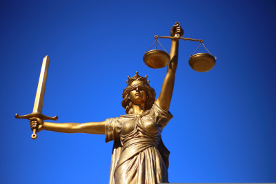 Justitia mit verbundenen Augen, Schwert und Waage vor blauem Hintergrund